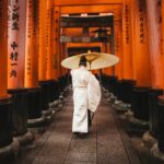 A person in traditional attire walks through the iconic torii gates at Fushimi Inari Shrine, Kyoto.
