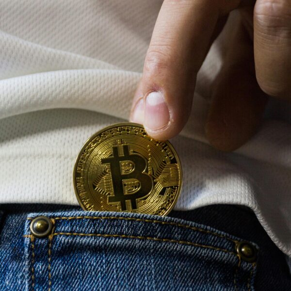 Close-up of hand putting Bitcoin in jeans pocket symbolizing cryptocurrency savings.
