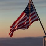 A vibrant US flag waves against a scenic sunset backdrop in Stowe, Vermont.