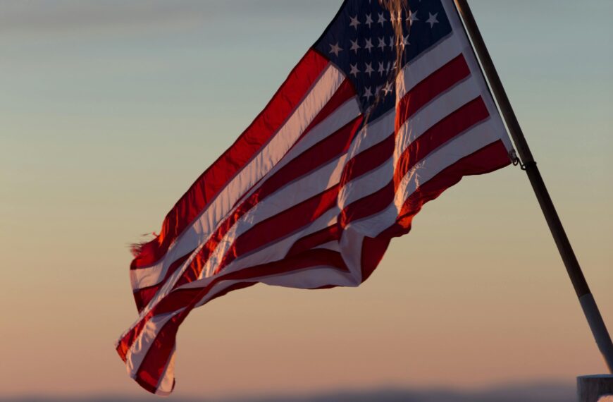 A vibrant US flag waves against a scenic sunset backdrop in Stowe, Vermont.